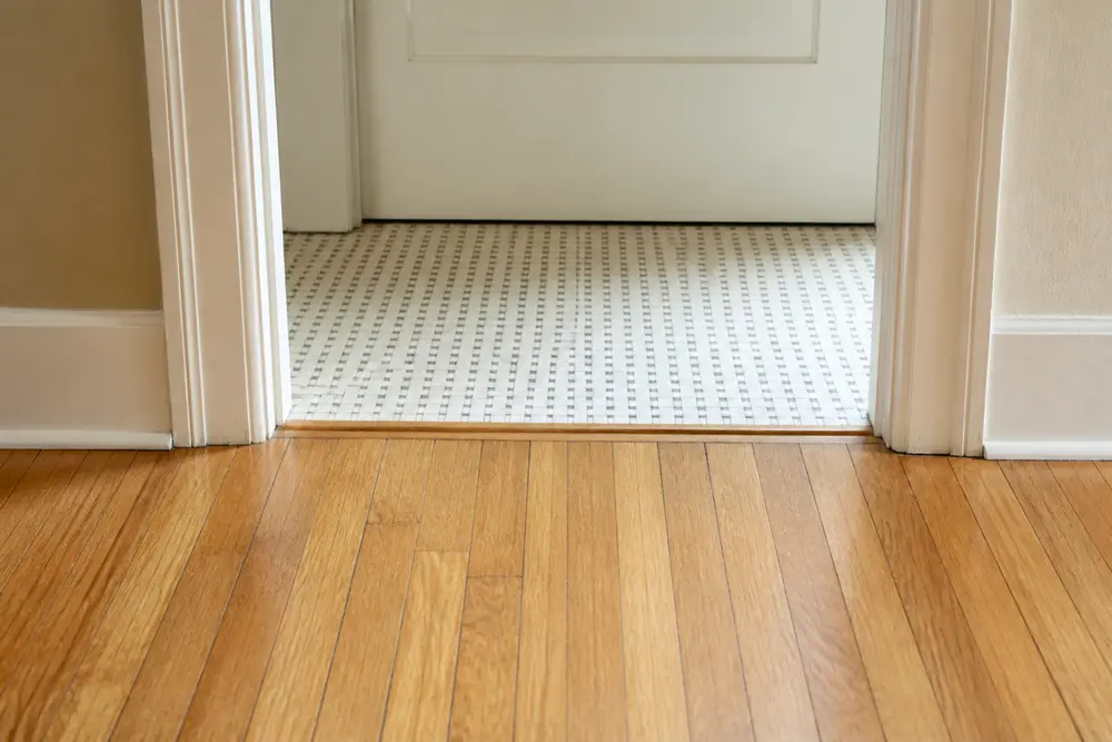 Oak flooring meeting small mosaic tile at a straight interior doorway transition.