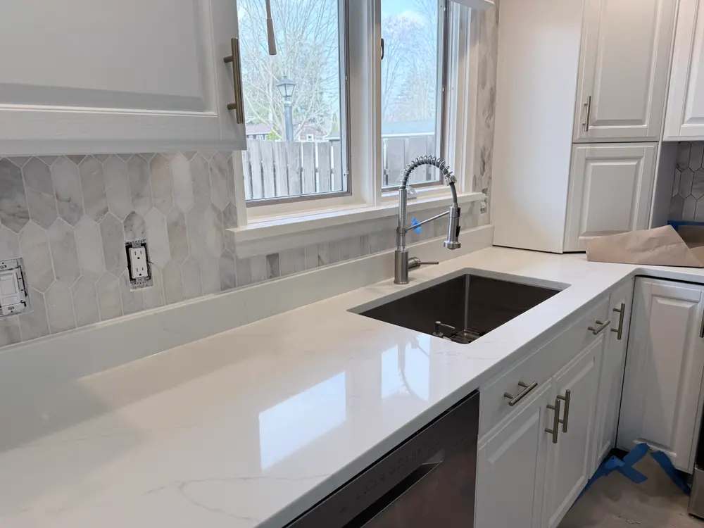 Marble backsplash around a kitchen window above a sink and pale countertop, installed by Livanzh.