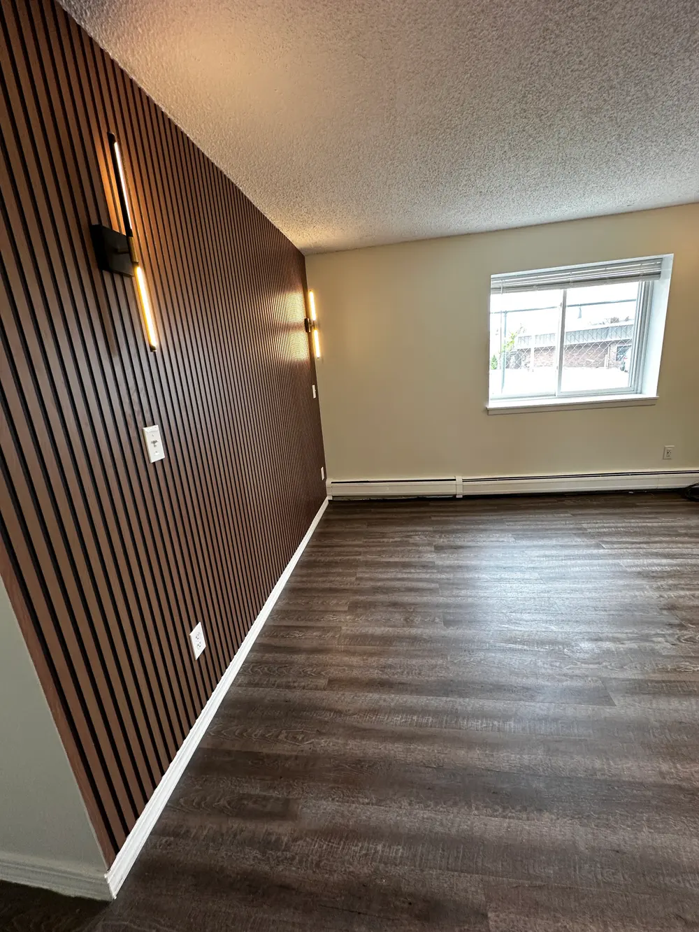 Room with a wood slat wall, wall lights, painted surfaces and wood-look flooring.